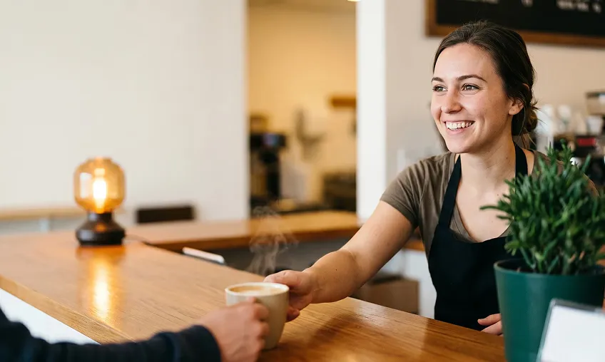 Barista serving a cup of coffee across a café counter